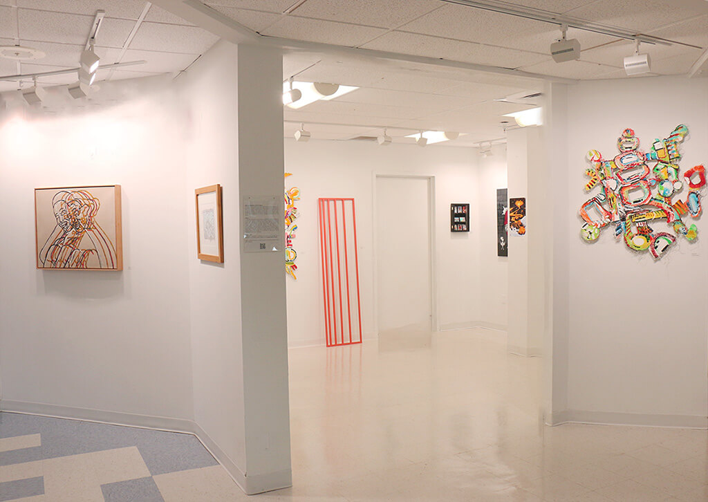 A wide-angle view of an art gallery space with several paintings and a sculpture.