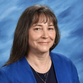 A portrait of a smiling woman wearing a blue blazer with a sky blue background